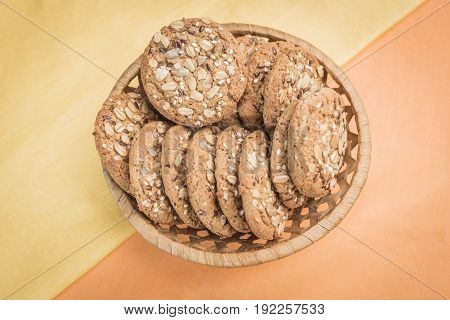 Homemade cookies with cereals and seeds in a wicker basket on a pear-yellow and light orange warm background top view