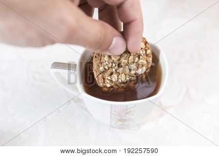 Hand dipping homemade cookies with cereals and sunflower seeds in a cup of tea on a white background