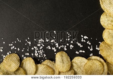 Crinkle cut potato chips on a blackboard. Tasty spicy potato chips with salt.Top view