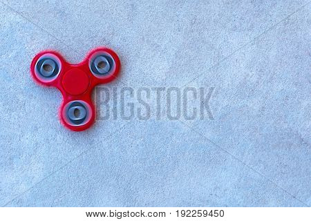 Red fidget spinner stress relieving toy on concrete background. Popular spinner gadget in 2017