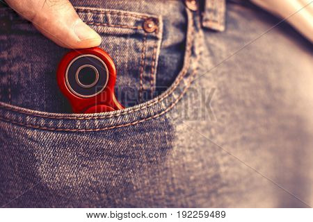 Caucasian man hides his red finger fidget spinner at jeans pocket. Popular spinner gadget in 2017.