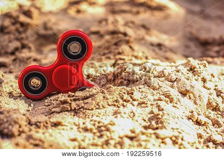 Top view of a red fidget spinner in the sand