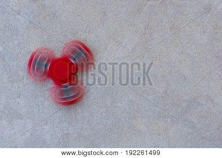 Red fidget spinner in motion stress relieving toy on concrete background.