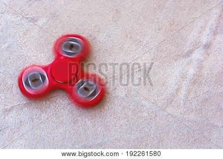 Red fidget spinner in motion stress relieving toy on concrete background.