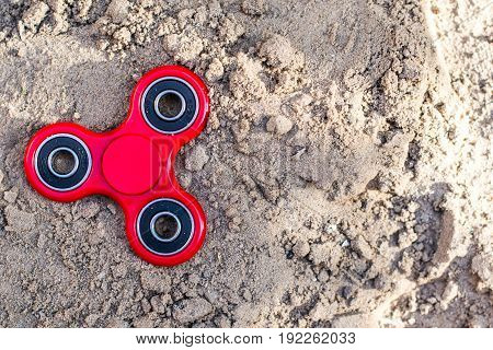 Top view of the popular red spinner gadget in 2017 against the background of sand. Modern red plastic spinner fidget game for young people.