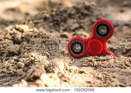 Popular red spinner gadget in 2017 against the background of sand. Modern red plastic spinner fidget game for young people