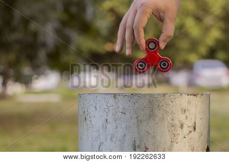 Closeup of a young caucasian man throwing a red fidget spinner in a garbage can on the background of nature. Popular spinner gadget in 2017.
