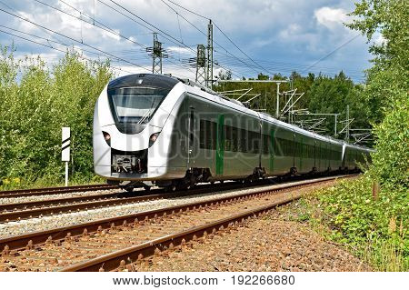 A modern electric regional train runs on a multi-lane track through natural surroundings