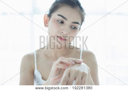 A beautiful woman asian using a skin care product moisturizer or lotion taking care of her dry complexion. Moisturizing cream in female hands .