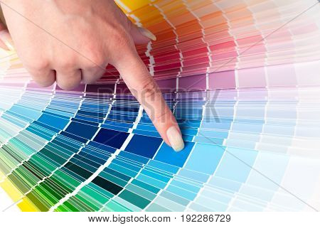 The person with a finger shows to the selected color in the palette for paint tinting. Colored catalog fan. The concept of choosing interior design