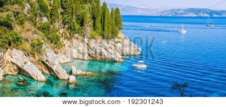 Rocky coastline covered by cypress and tourest boats in azure water, near Kalami, Corfu. Banner