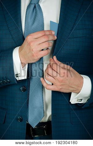 hands hiding blank business or bank card in elegant blue formal suit jacket with white shirt and tie. Economy credit ecash banking ethics and information