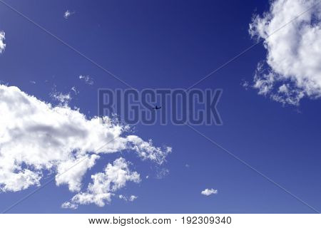 Airplane in the blue sky, between two clouds. Space for text.