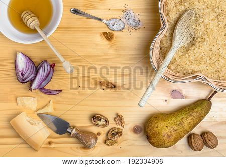 Ingredients for cooking an italian savory meal. Raw parboiled rice pear walnuts honey onions salt and parmesan over rustic wooden background. Top view. Copy space.