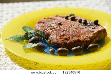 Tuna steak served with olives, basil and capper in yellow plate in blurry background