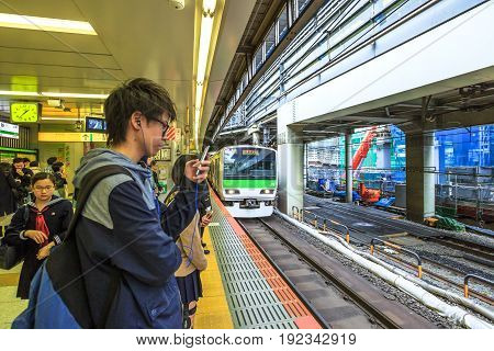 Tokyo, Japan - April 17, 2017: a boy looks at his smarth phone while waiting the Yamanote Line, the most important train line in Tokyo. The Yamanote is a JR line and a circular ring around city center