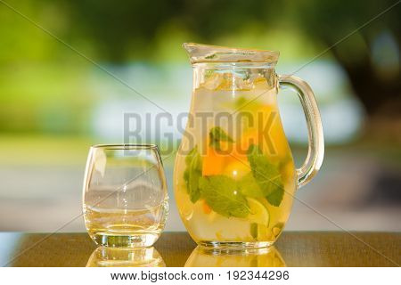 Jug of non-alcoholic drink and a glass on a table with a blurred background.