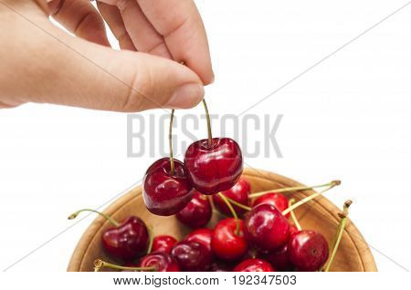 female fingers take the cherries from a wooden dish on white background