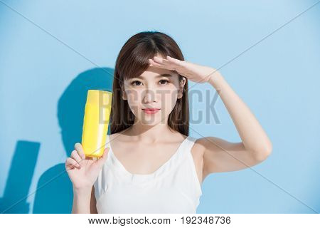 woman take sunscreen and look somewhere on blue background