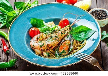 Italian pasta spaghetti with seafood langoustine mussels squid scallops shrimp Parmesan cheese fresh basil and tomatoes on rustic wooden background. Mediterranean food. Top view