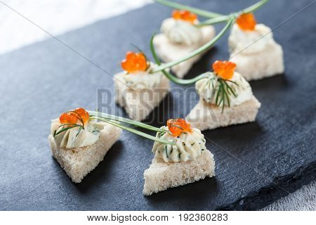 Appetizer canape with red caviar and cream cheese on stone slate background close up. Delicious snacks sandwiches crostini brushetta antipasti on party or picnic time. Top view