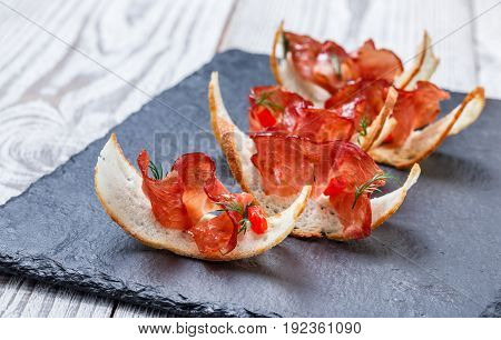 Appetizer bruschetta with jerky prosciutto on thinly sliced ciabatta bread on stone slate background close up. Delicious snacks sandwiches crostini antipasti. Top view
