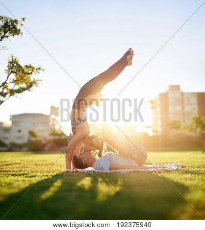 Active flexible couple doing acro yoga on the grass at sunset, trust bonding loving relationship exercise together