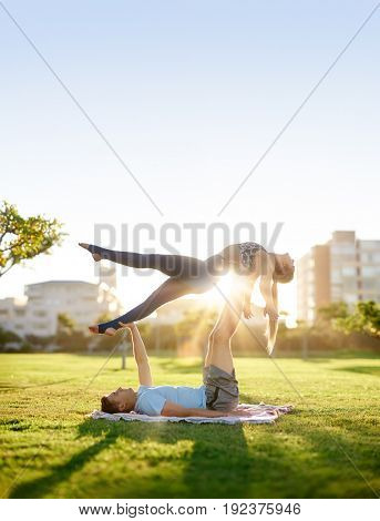 Couple exercise in the park, practicing couples acro yoga building trust strength balance and flexibility plenty of copy space with sun flare
