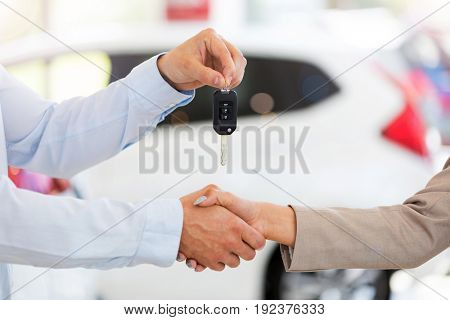 Car salesman handing car keys to woman in showroom
