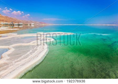 Very salty water glows with turquoise light. Reduced water in the Dead Sea. The evaporated salt has developed into fantastic patterns. The concept of ecological and medical tourism