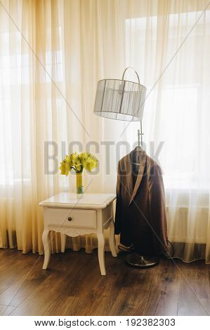 Yellow flowers in bride boquete with yellow stripe. Bouqquete standing on a white retro table near brown man wedding suite in style hotel. Close up view. Broun yellow color.