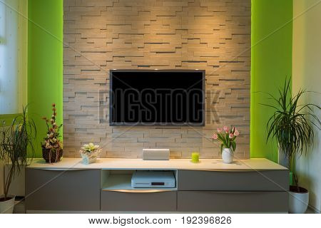 Modern living room interior - tv mounted on brick wall with black screen and ambient light.