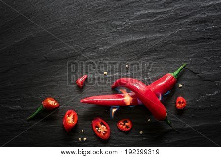 Red spicy chili peppers over dark slate with fire. Food background overhead view.