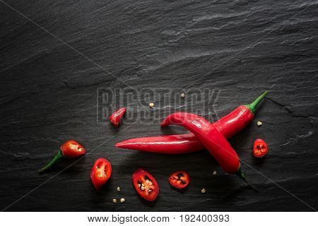 Red spicy chili peppers over dark slate. Food background overhead view.