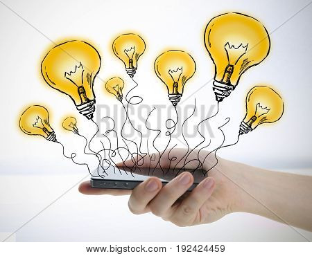 Close up of woman's hand holding smartphone with abstract drawn light bulb balloons on light background. Creative ideas concept