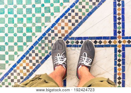 Feet selfie from upper view of man traveler in sneaker during a tour trip around the world. Souvenir photo of multicolor museum floor made of small tiles. Tourist take a photo of his own leg.