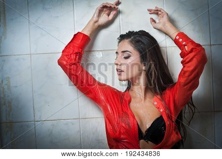 Cute brunette woman with perfect body posing in erotic pose under shower with wet hair and transparent  red shirt, perfect voluptuous body.Portrait of a joyful girl in wet shirt