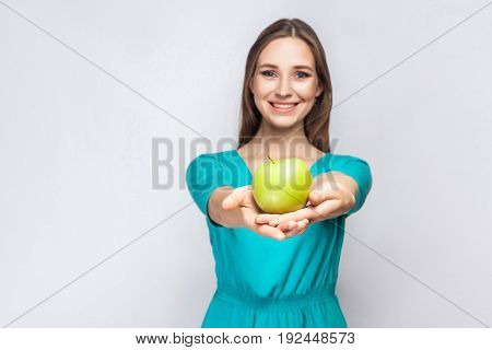 Young beautiful woman with freckles and green dress holding apple and sharing with smile. studio shot isolated on light gray background.