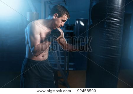 Man in black handwraps exercises with bag in gym
