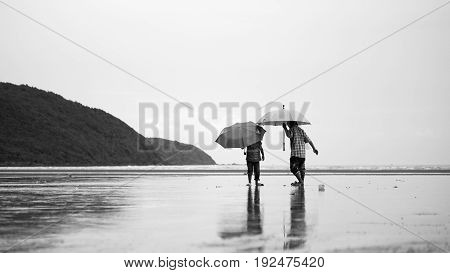brother and sister hoding on a umbrella walking to the sea.
