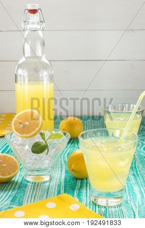 lemonade or limonchello in yoke stopper bottle beverage in glasses sherbet glass with ice cubes lemon fruits on turquoise colored wooden table