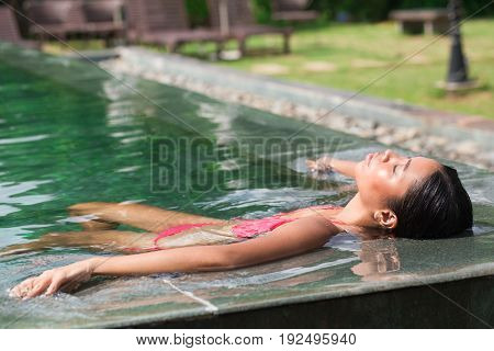 Closeup of content young attractive Asian woman lying on water at edge of swimming pool