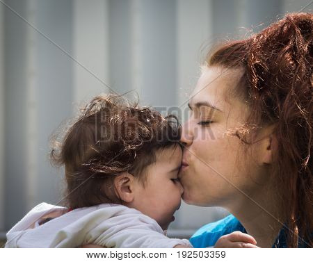 A mother showing her affection by kissing him on the forehead.