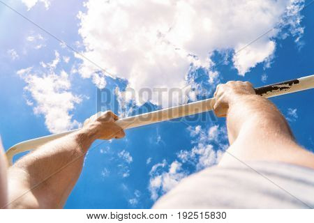 First-person view of the horizontal bar. The guy pulls up on the bar. Workout outdoors. Blue sky on blackground.