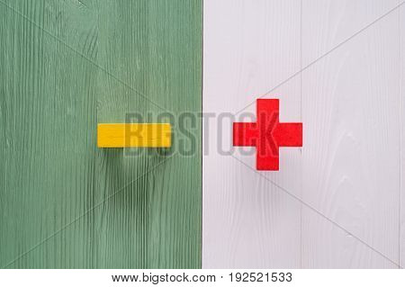 The concept of opposites plus and minus flat lay. Wooden figures plus and minus on a wooden background. Plus versus minus with copy space top view.