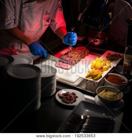 Hand with knife and fork cutting tasty grilled steak on board in hotel restaurant