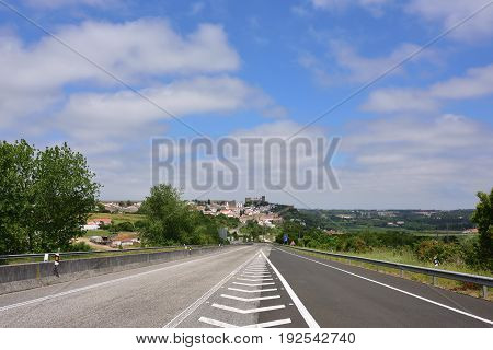 Tar road to the medieval city of Obidos. Cityscape of the town with medieval houses wall and the Albarra tower. Obidos is a medieval town still inside castle walls and very popular among tourists.