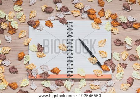 Spiral notebook with pen and maple leaves on wood background in autumn