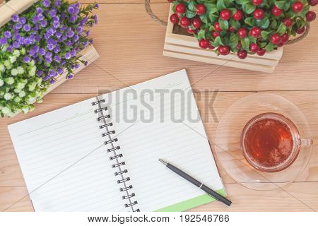 Spiral notebook with tea and flowers on wood background
