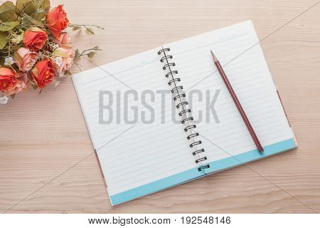 Spiral notebook with pencil and artificial flowers on wood background